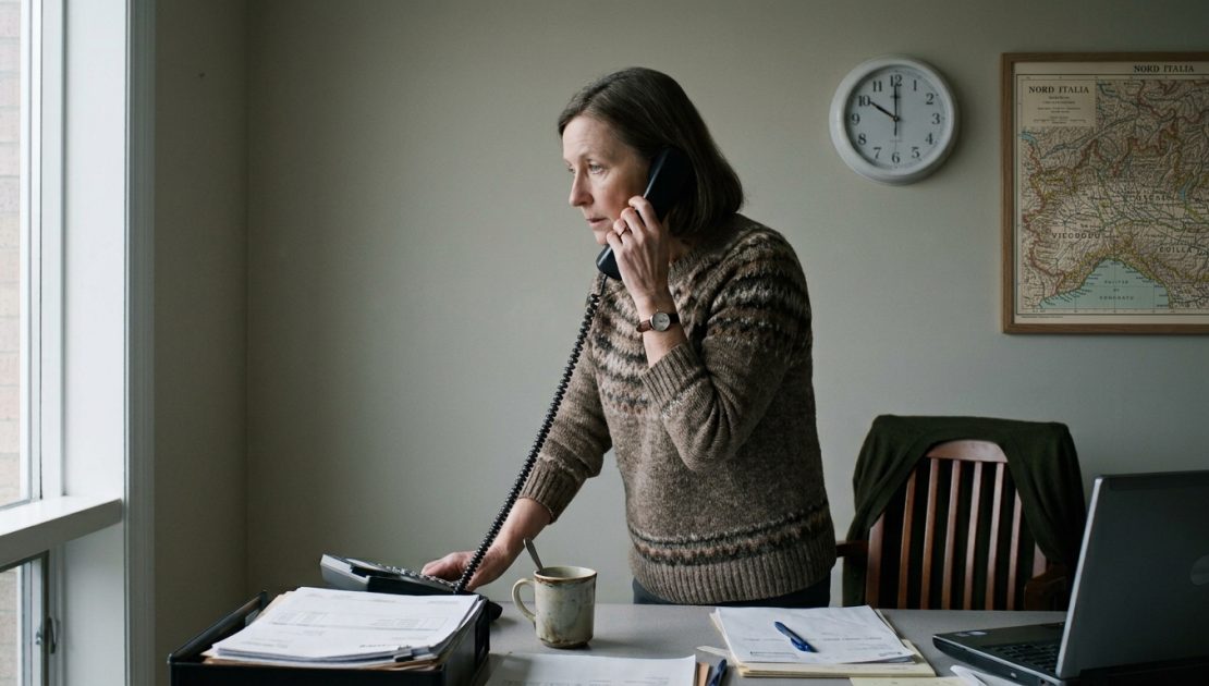 Furto credenziali email aziendale: una donna al telefono in un ufficio di provincia, la mano appoggiata alla scrivania, l'orologio sulle dieci