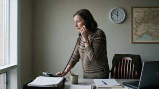 Furto credenziali email aziendale: una donna al telefono in un ufficio di provincia, la mano appoggiata alla scrivania, l'orologio sulle dieci